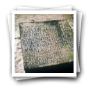 Sobre a areia da praia, um bloco de pedra com [uma] inscrição